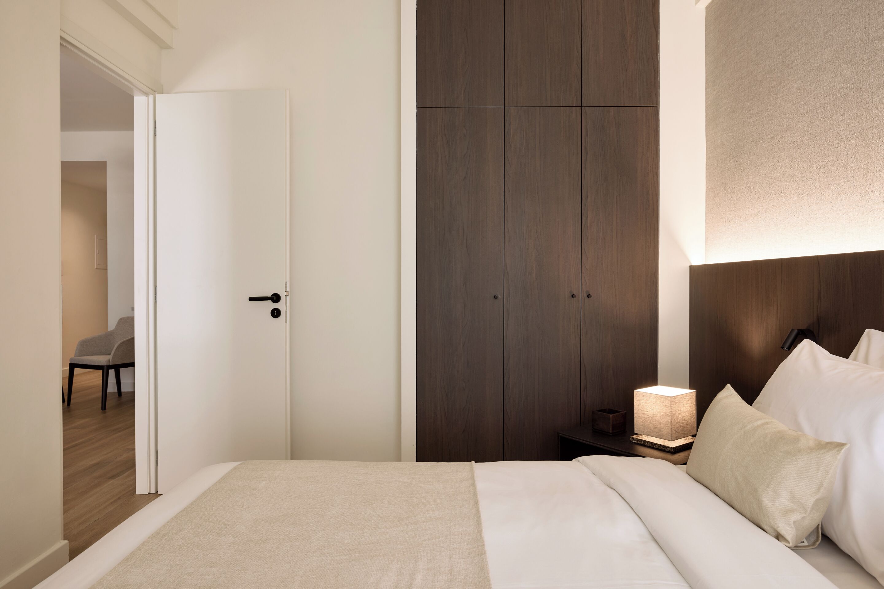 Une chambre à coucher avec un lit, une table de chevet avec une lampe, une armoire et une chaise au fond de la pièce.