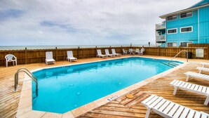 Una piscina con muelle de madera, sillas de descanso y cerramiento de madera.
