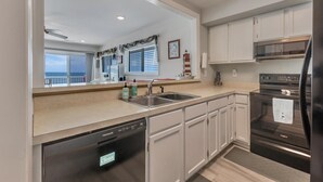 Una cocina moderna con lavavajillas, electrodomésticos de acero inoxidable y un amplio ventanal con vistas a un balcón.