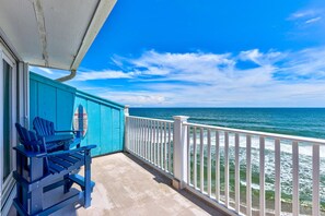 Ein Balkon mit Meerblick, ein blauer Adirondack-Stuhl und ein weißes Geländer.