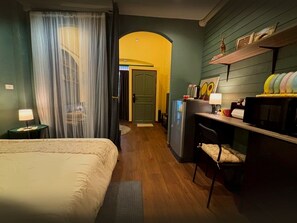 Pieni hotellihuone, jossa on sänky, työpöytä ja pieni keittiönurkkaus.