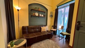 A cozy living room with a leather sofa, a small round rug, a side table with a lamp, and a bookshelf against the wall.