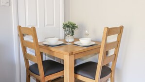 A dining table with four wooden chairs, two white bowls, a wine glass, and a potted plant. - Sunnyfield Cottage (Coulsdon)