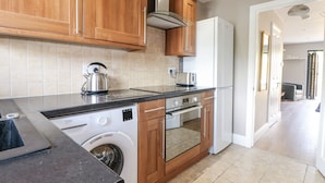 A kitchen with wooden cabinets, a built-in oven, a washing machine, and a refrigerator. - Sunnyfield Cottage (Coulsdon)