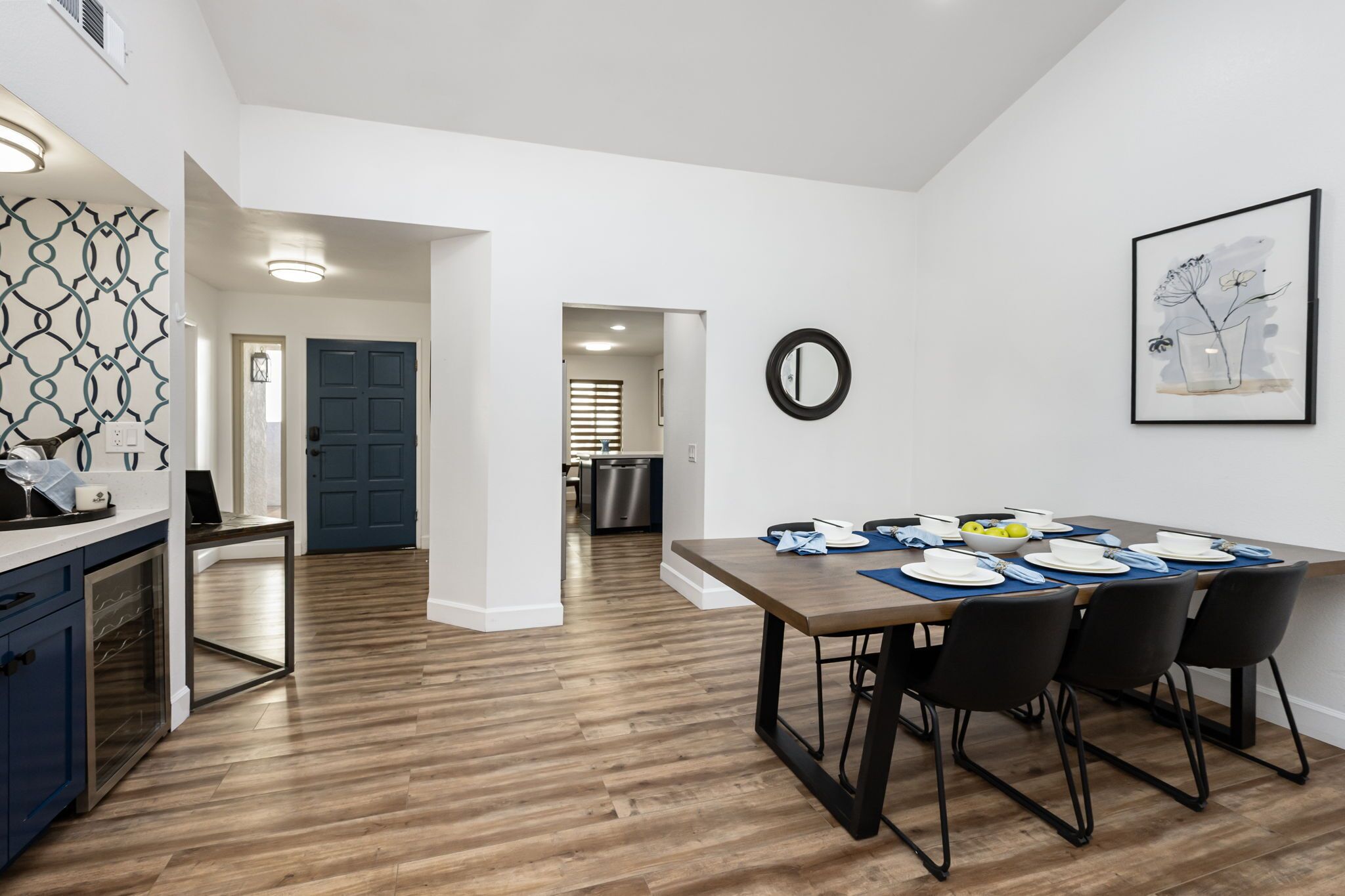 Une cuisine moderne avec un plancher en bois, un coin repas avec une table dressée pour quatre personnes, et une porte bleue en arrière-plan.