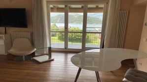 Una habitación moderna con un gran ventanal corredero que da a un balcón con vistas panorámicas a un lago y montañas.