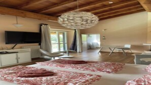 Una habitación amplia con techo de madera, una lámpara de araña grande, una cama con colcha estampada, un escritorio y una silla.