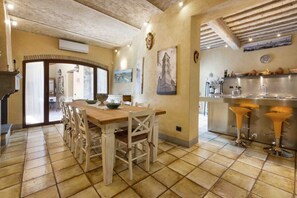 Un'area pranzo con tavolo e sedie in legno, una cucina con lavello in acciaio inossidabile e un pavimento piastrellato.