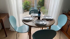 A dining area with a round table set for four, light blue chairs, and a bottle of wine. - 2 Bed-sleeps 4-parking-pets-10 min Walk to Beach (Falmouth)
