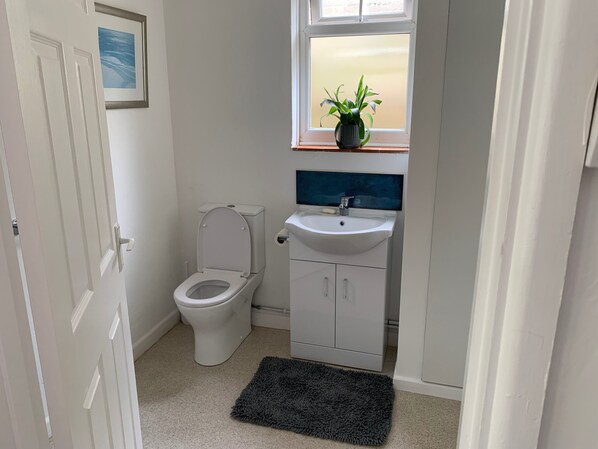 A small, clean bathroom with a toilet, sink, and a window with a plant. - 2 Bed-sleeps 4-parking-pets-10 min Walk to Beach (Falmouth)