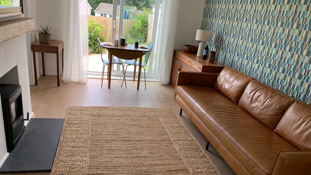 A living room with a brown leather sofa, a woven rug, a wooden coffee table, and a patterned wall. - 2 Bed-sleeps 4-parking-pets-10 min Walk to Beach (Falmouth)