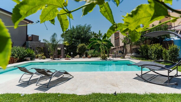 A swimming pool with lounge chairs, surrounded by greenery and buildings.