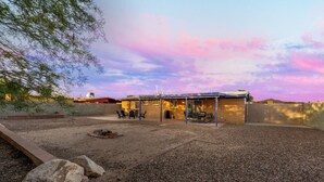 A covered outdoor patio with a fire pit, seating area, and a building with a flat roof.