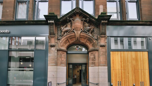 Une entrée d’immeuble avec une arche en pierre, une porte en bois et une vitrine.