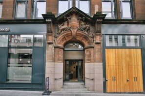 A building entrance with a stone archway, a wooden door, and a glass storefront. - Student Only George Street (Glasgow)