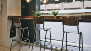 Un espace bar moderne avec trois tabourets de bar en métal, un comptoir en bois et des lampes suspendues.