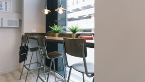 Une cuisine moderne avec deux tabourets de bar, une fenêtre donnant sur des immeubles et des lampes suspendues.
