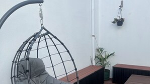 Une terrasse en bois avec un fauteuil suspendu, une table et des plantes en pot.