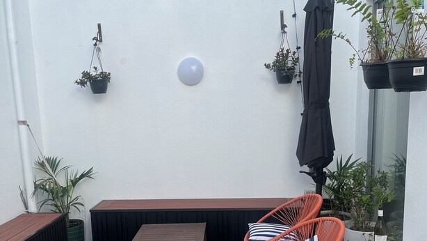 Une terrasse en bois avec un banc et deux chaises à rayures, des guirlandes lumineuses et des plantes en pot.