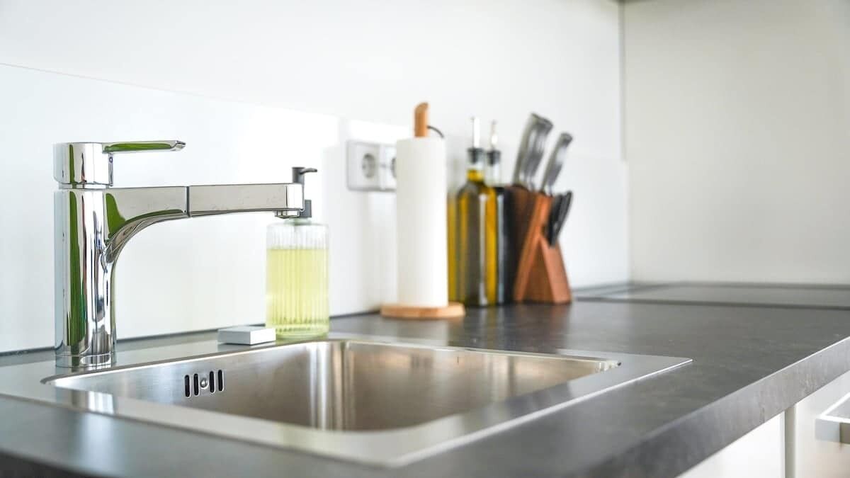 Eine moderne Küche mit einer Spüle aus Edelstahl, einem Wasserhahn und einem Glas mit gelber Flüssigkeit.
