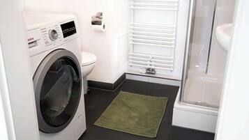 Une salle de bain compacte équipée d’un lave-linge Bosch, de toilettes et d’une cabine de douche en verre.