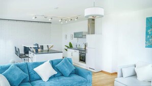 A modern kitchen with white cabinets, a built-in oven, and a dining area with a blue sofa and white cushions. - JH Apartments Ingolstadt | Penthouse Altstadt (Ingolstadt)