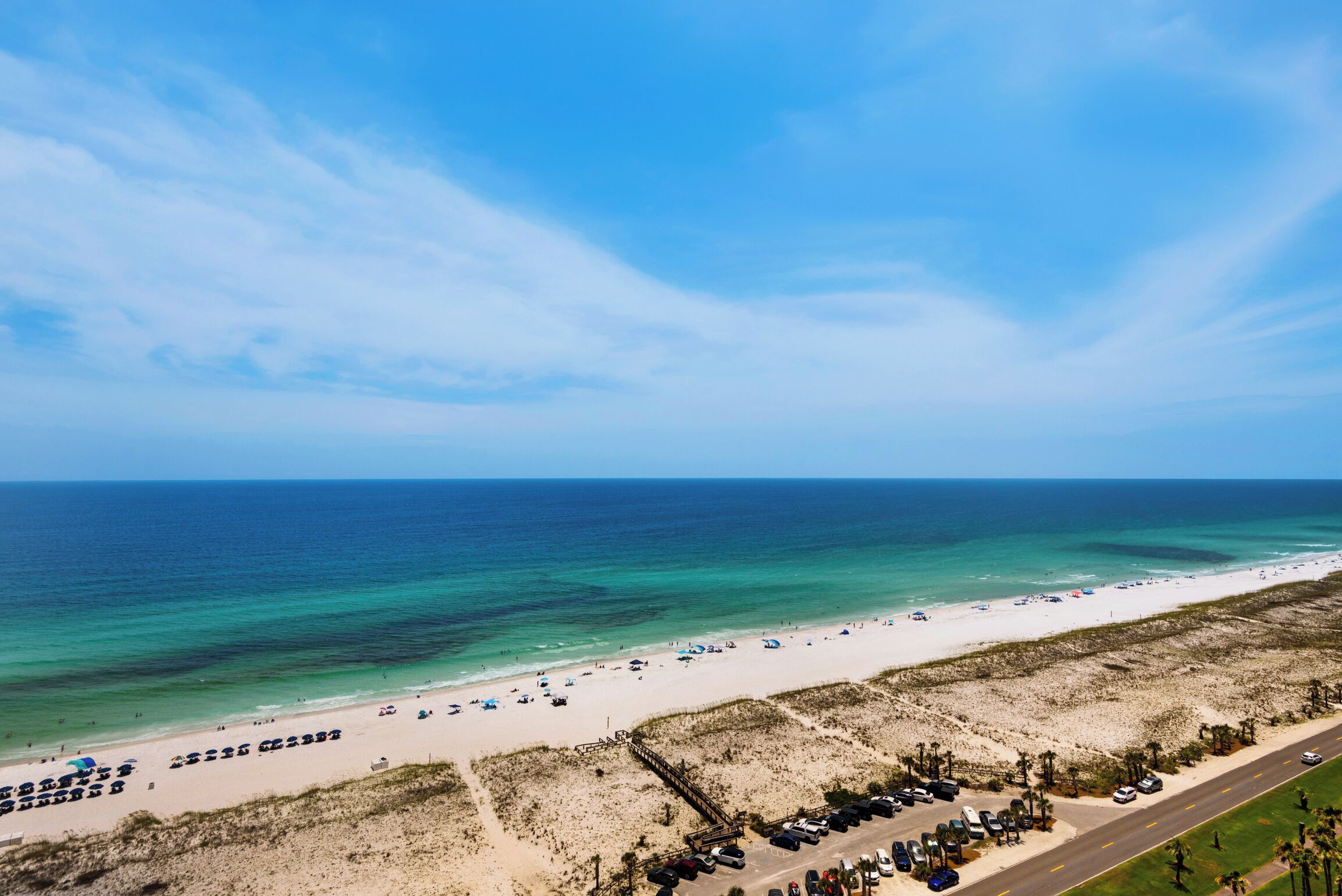 An aerial view of a beach with a parking lot and a road.