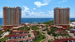 A high-rise hotel with a central courtyard, multiple parking areas, and a view of the ocean.