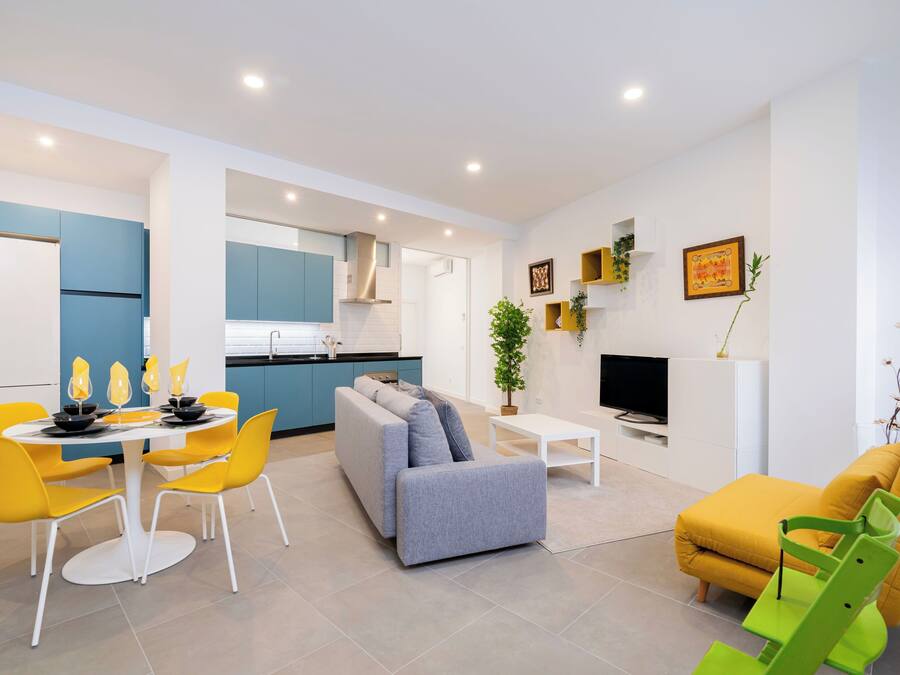 Un salon moderne avec un canapé, des fauteuils jaunes, une table à manger et une cuisine en arrière-plan.