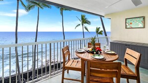 Ein Balkon mit einem Holztisch für zwei Personen, Blick auf einen Strand mit Palmen und den Ozean.