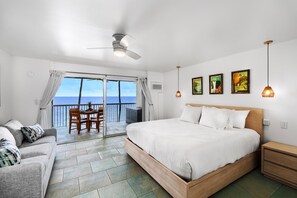 A bedroom with a large bed, a ceiling fan, a nightstand, and a view of the ocean through a sliding door. - Kona Magic Sands#313:Top Floor,Direct Beachfront, Rarely Available Lanai unit (Kailua Kona)