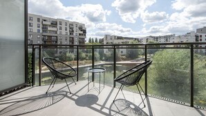 Parvekkeella on kaksi tuolia ja pieni pöytä, ja sieltä avautuu näkymä kaupunkimaisemaan, jossa on moderneja rakennuksia ja vesistö.