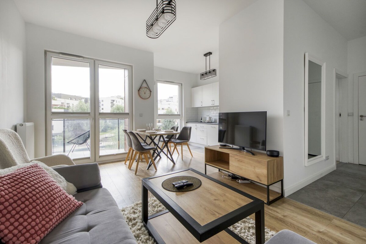 Ein modernes Wohnzimmer mit Sofa, Couchtisch, Fernseher, Essbereich mit Stühlen und einer Küche im Hintergrund.