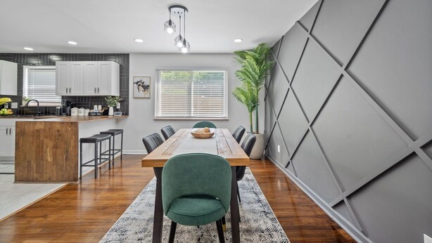 Une cuisine moderne avec des meubles blancs, un îlot central en bois et un coin repas comprenant une table en bois et des chaises vertes.