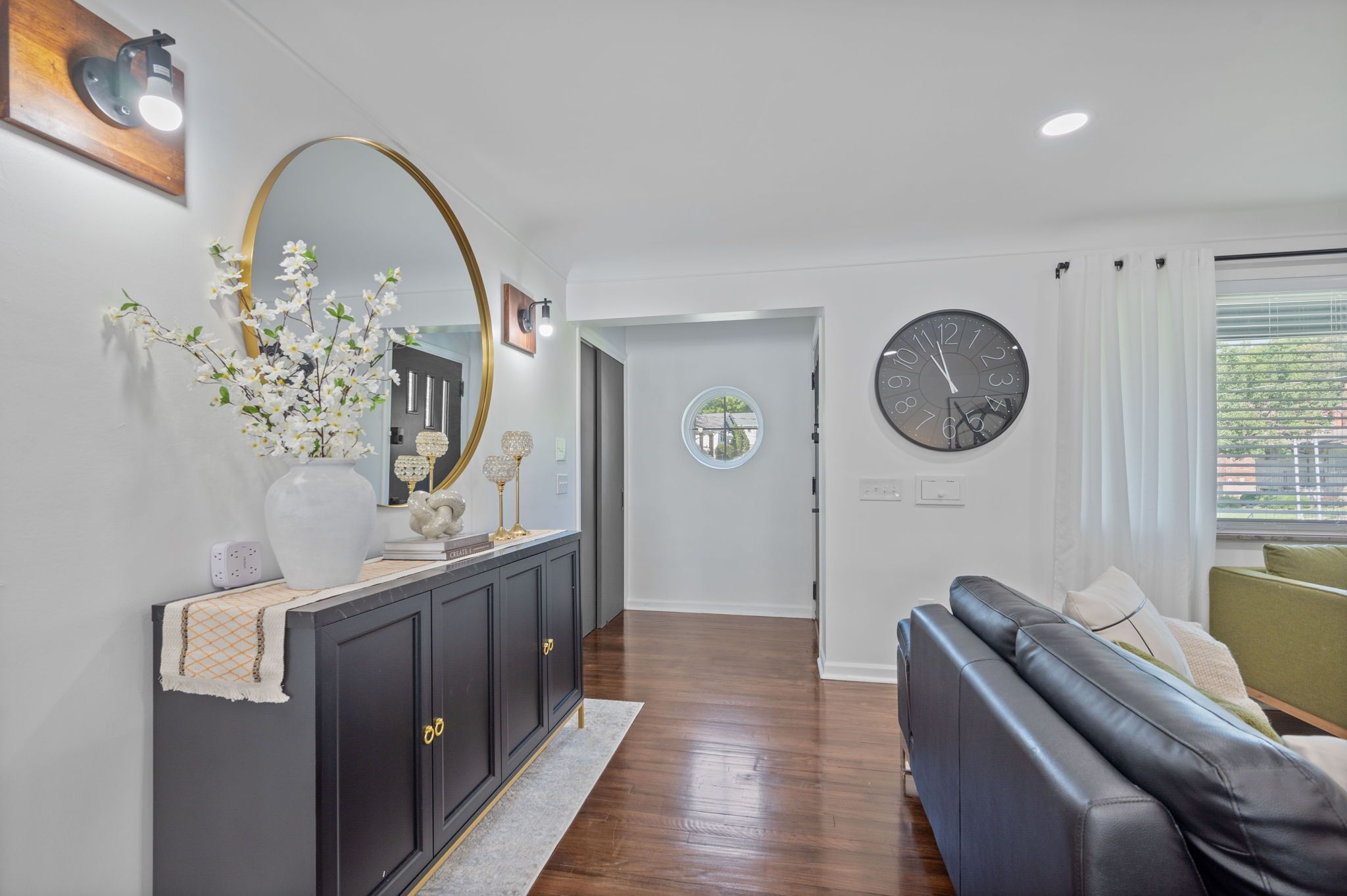 Un salon moderne avec un canapé en cuir foncé, une horloge ronde et un vase de fleurs posé sur une console.