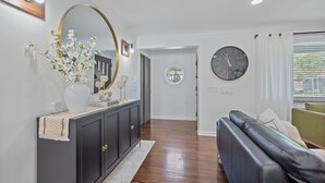 Un salon moderne avec un canapé en cuir foncé, une horloge ronde et un vase de fleurs posé sur une console.