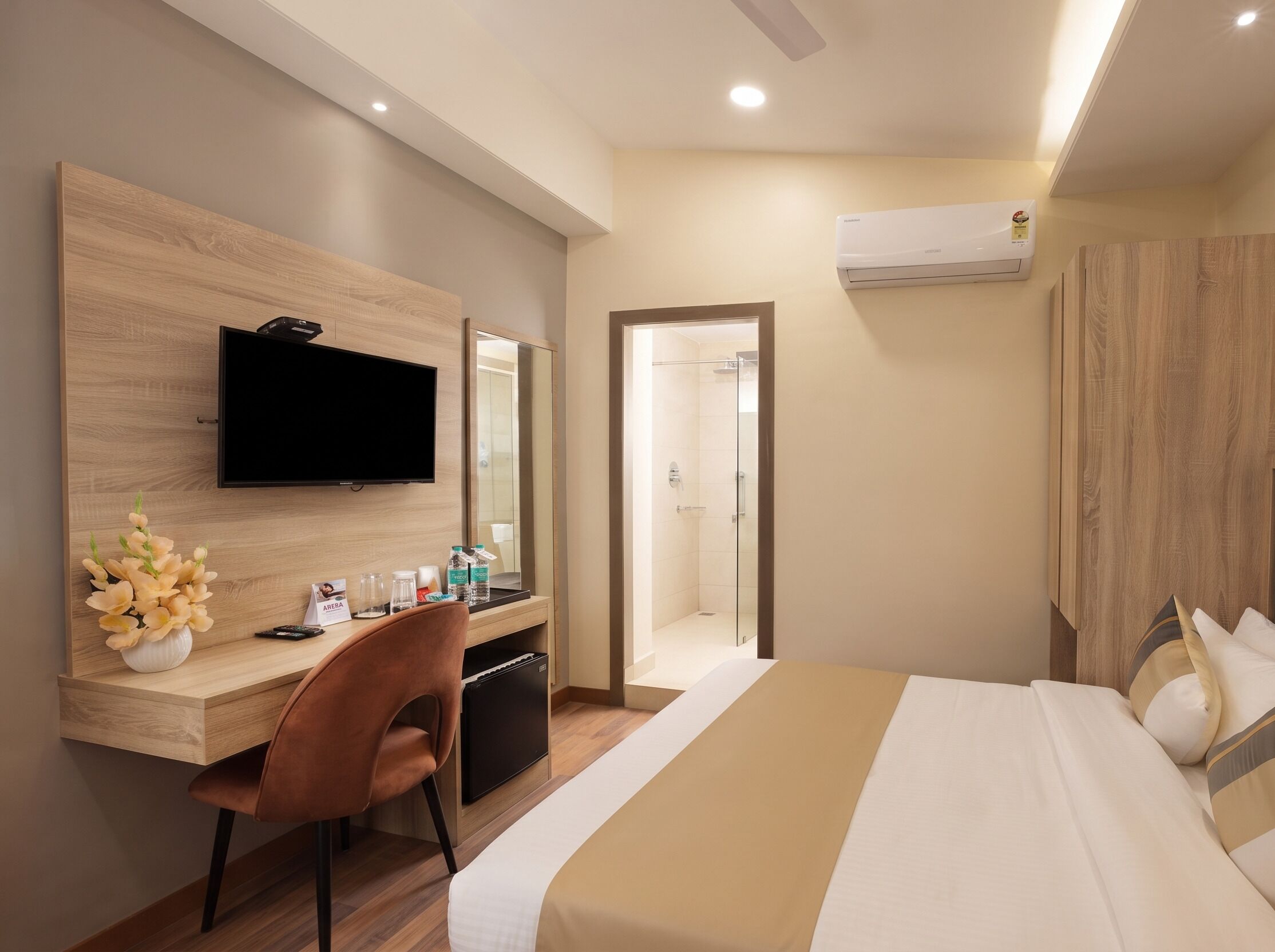 A hotel room with a bed, a desk with a chair, a television, a mirror, and a shower area.