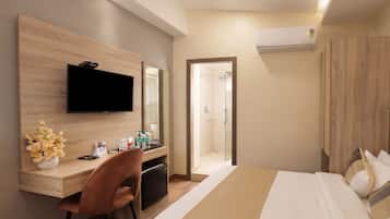 A hotel room with a bed, a desk with a chair, a television, a mirror, and a shower area.
