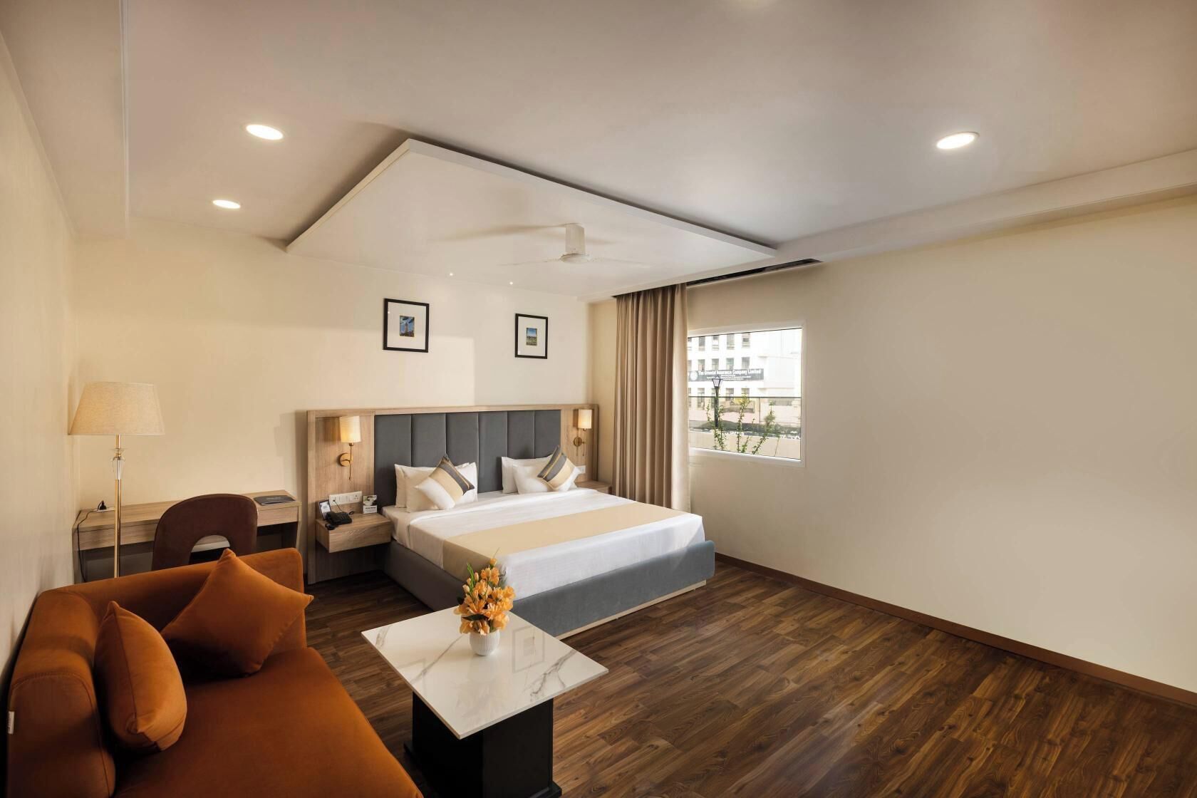 Una habitación de hotel con cama, escritorio, silla, lámpara y ventana con cortinas.