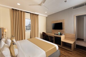 Habitación de hotel con cama, escritorio, silla, televisión y vista a la ciudad.