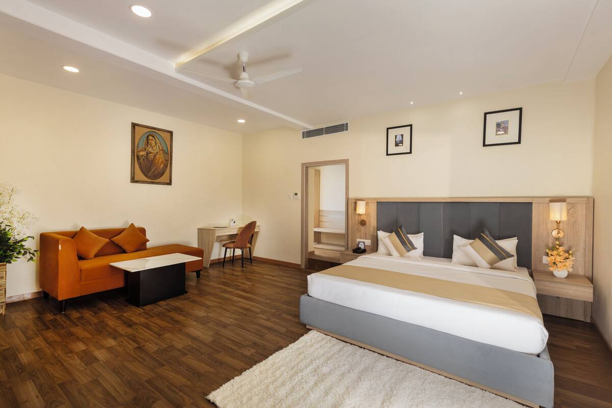 A modern hotel room with a large bed, a sofa, a desk, and a ceiling fan.
