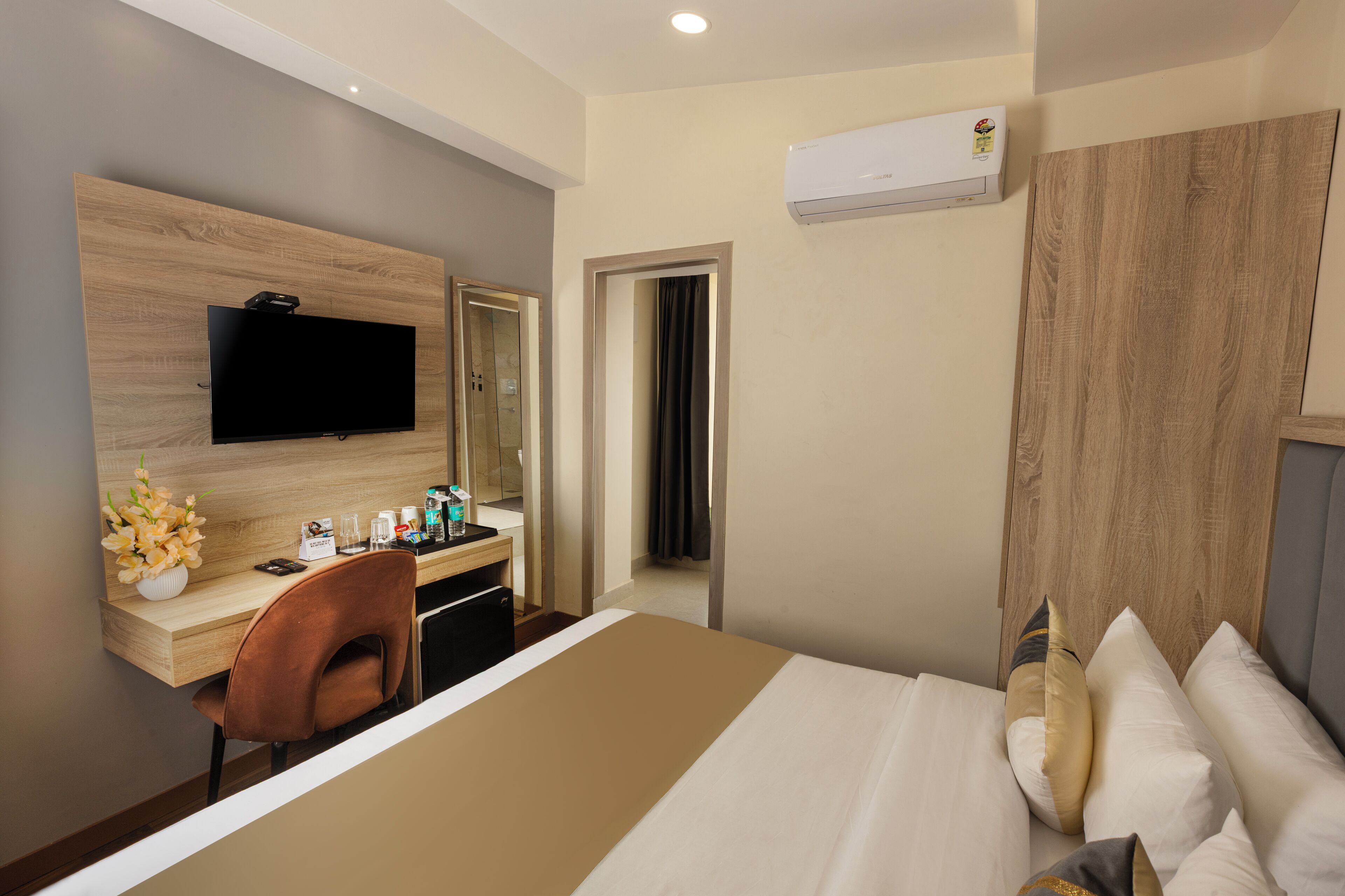 A hotel room with a bed, a desk with a chair, a television, and a bathroom door.
