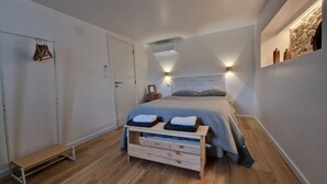 A bedroom with a bed, bedside tables, a wooden bench, a wardrobe, and a wall-mounted shelf with decorative items.