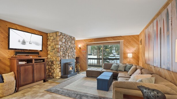 A cozy living room with a stone wall, a fireplace, a large TV, and a sofa. - 3 Bedroom Kirkwood Condo Base Camp 3 Condo (Kirkwood)