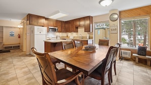 A kitchen with wooden cabinets, a dining table with chairs, a microwave, and a refrigerator. - 3 Bedroom Kirkwood Condo Base Camp 3 Condo (Kirkwood)