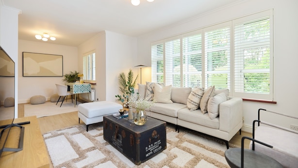 A spacious living room with a white sofa, a coffee table, and a large window with blinds. - The Lindens Garden Retreat (Taplow)