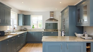 A modern kitchen with blue cabinets, a stainless steel range hood, and a window providing natural light. - The Lindens Garden Retreat (Taplow)