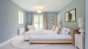 A bedroom with a bed, a chair, a nightstand, and a window with curtains. - The Lindens Garden Retreat (Taplow)