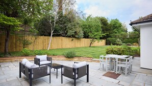 An outdoor patio with a seating area, a table, and a view of a well-maintained lawn and trees. - The Lindens Garden Retreat (Taplow)