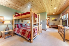 A bunk bed room with a wooden ceiling, a desk, and a lamp.